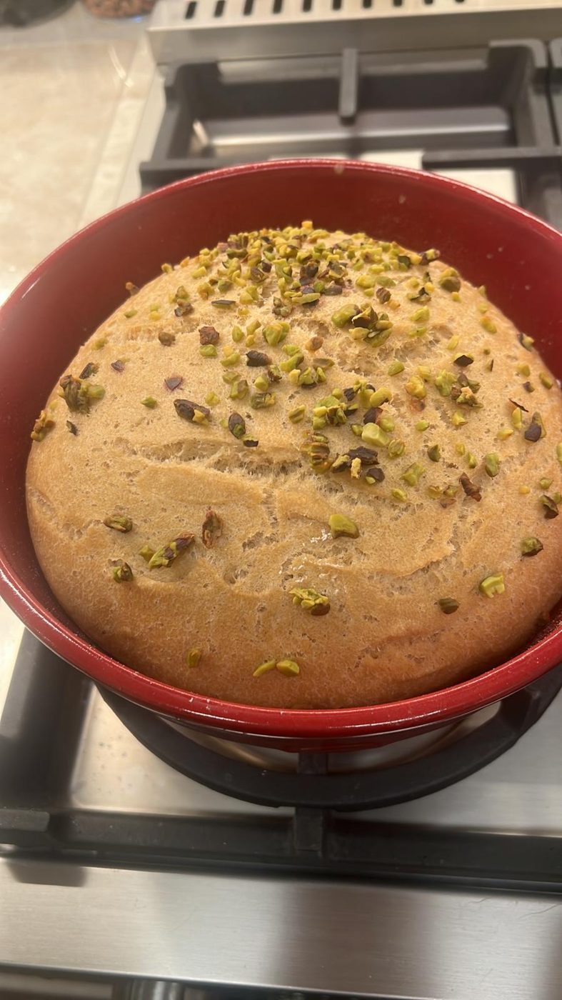 A round loaf of homemade bread topped with pistachios, in a red baking dish